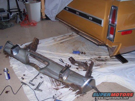Gold 1972 Ford Ranchero rear quarter panel with detached chrome bumper on a white tarp
