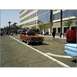 2007 Ford Ranchero - An orange pickup truck drives down a street with a crowd of people and buildings in the background.