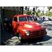 2007 Ford Ranchero - A bright red pickup truck is parked on a street, with people and trees in the background.