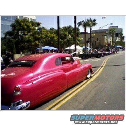 Pink custom coupe with chrome bumper and whitewall tires, seen from the rear quarter angle on a street