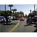 2007 Ford Ranchero - A red classic car drives down a street during a parade, with palm trees and buildings lining the route.
