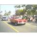 2007 Ford Ranchero - A red coupe utility vehicle with a hood scoop drives down a street lined with palm trees and spectators.