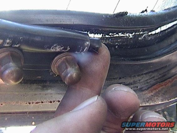 Close-up of a person's hand touching a car's door seal near some bolts
