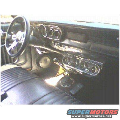Car interior with black leather seats, chrome steering wheel, and dashboard gauges. Text 'SUPERMOTORS' visible