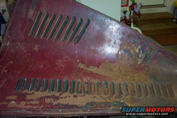 Rusted red car hood section with horizontal louvers on the left and right sides