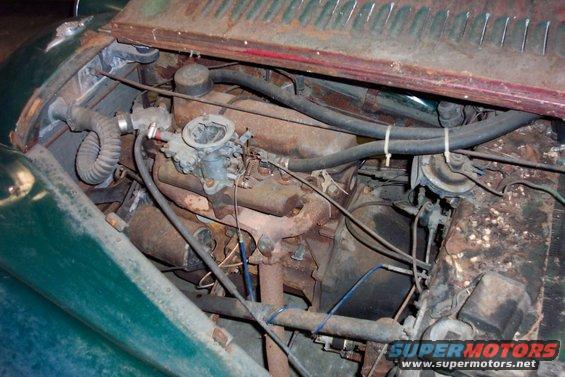 Close-up of a rusty car engine bay with a carburetor and hoses