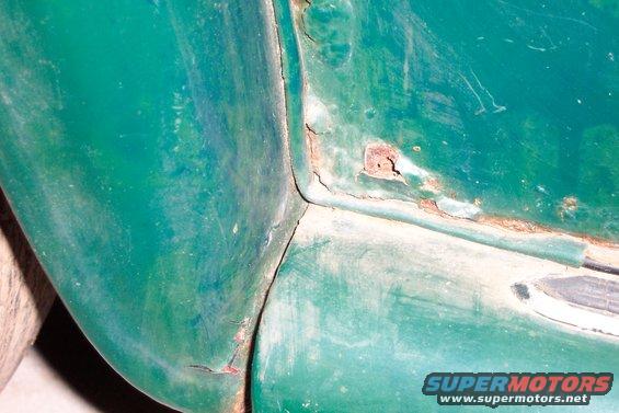 Green car body panel showing rust damage at a seam