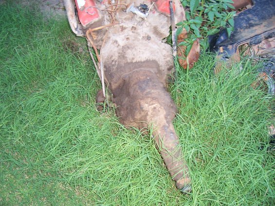 rusted car transmission and engine components lying in green grass