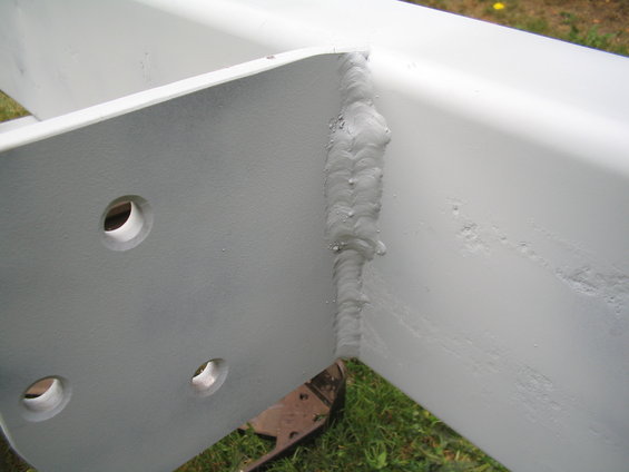 Close-up of a white painted metal corner with visible welds and three bolt holes