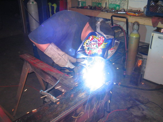 Person welding a metal beam on a red sawhorse in a workshop