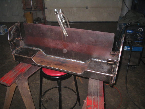 Custom fabricated bumper part on sawhorses with welding equipment in background