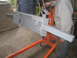 1979 Ford Bronco - A gray bumper part is being worked on, suspended by an orange engine hoist in a workshop.