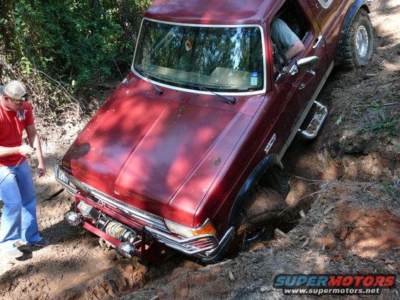 Red Ford Bronco with winch stuck in a dirt ditch, driver visible inside