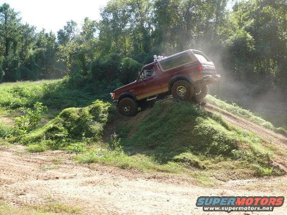 Red Ford Bronco climbing a dirt hill with trees in the background