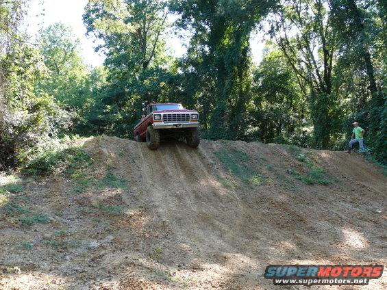 Red 1980s Ford Bronco climbing a dirt hill