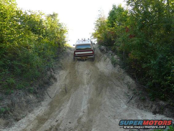 Off-roader going up a steep dirt hill, trees on both sides