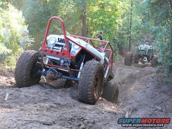Off-road vehicle with red roll cage on muddy trail
