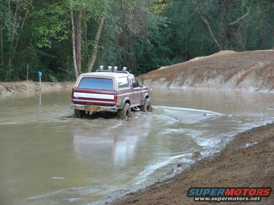 1988 Ford Bronco driving through a muddy water obstacle, rear view