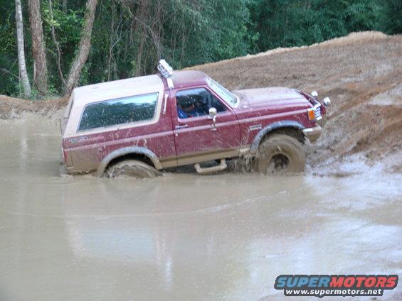 Maroon Ford Bronco with a tan top stuck in mud, viewed from the front-right