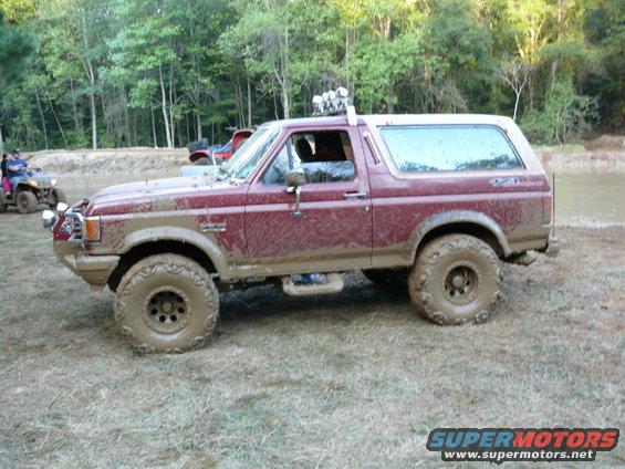 Maroon 1988 Ford Bronco with lifted suspension and off-road tires covered in mud