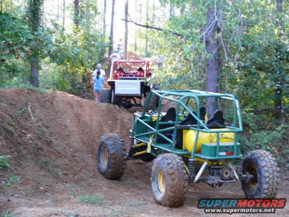 Green buggy with yellow tank climbing dirt hill, red buggy behind it