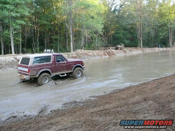 Maroon Ford Bronco driving through mud with roof-mounted lights