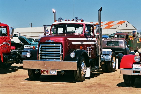 Maroon and white GMC semi-truck front view with chrome grille and dual exhaust stacks