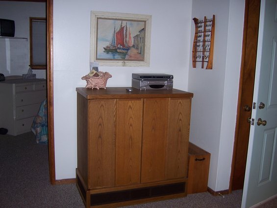 Interior shot of a room with a wooden cabinet, a painting of sailboats, and a dresser in the background
