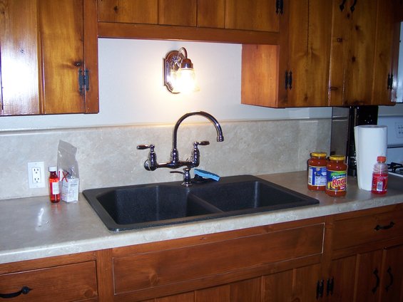 Double kitchen sink with chrome faucet, jars of sauce, and paper towels on a countertop