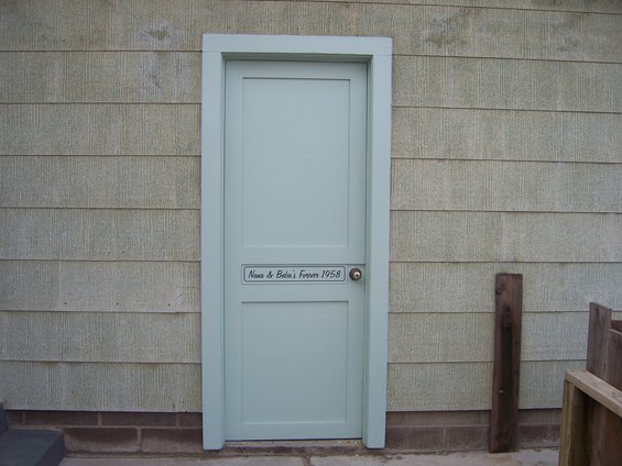 Light blue door on a house with horizontal siding. Plaque reads 'Nana & Bubba's Forever 1958'