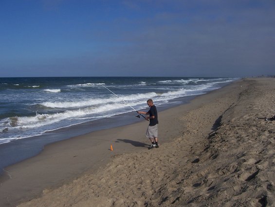 Man fishing on a sandy beach with waves crashing