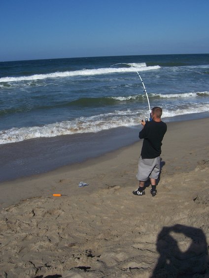 Man fishing with a rod and reel on a sandy beach with waves in the background