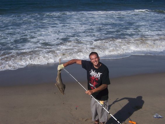 Man holding a fish on a sandy beach with waves in the background