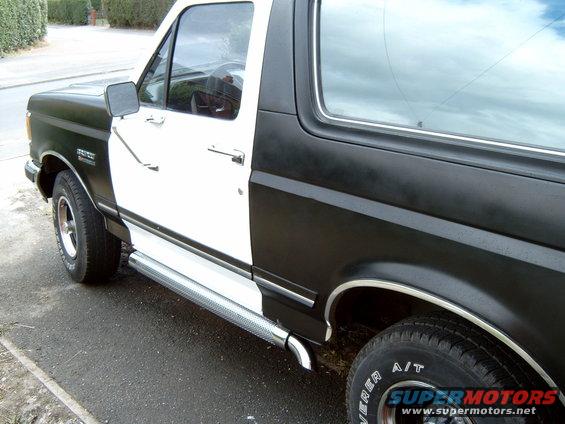 Two-tone black and white Ford Bronco, side view, showing chrome running boards and A/T tires