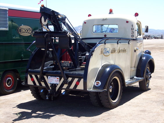 Cream and black tow truck with "A Fordable Service" text, 1938 badge visible