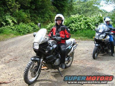 Black BMW motorcycle with rider in red jacket on dirt road