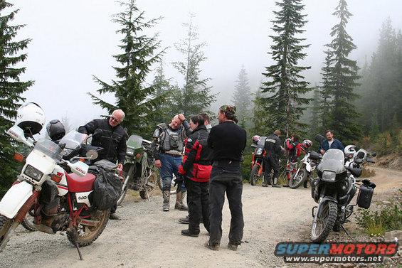 Group of people with motorcycles on a dirt road in a forest