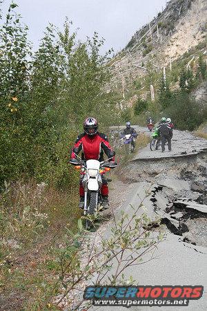 Motorcycles navigate a damaged mountain road with debris and landslides