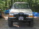 1979 Ford Bronco - This tan SUV features a prominent winch and bull bar on its front end, set against a wooded background.