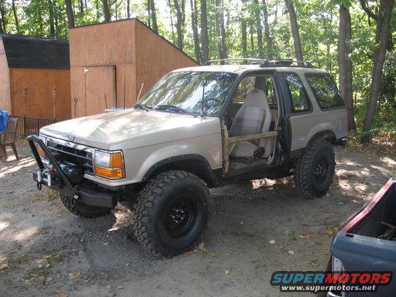 Tan Ford Bronco II with aftermarket bumper and winch, lifted suspension, and off-road tires. Driver's door is open