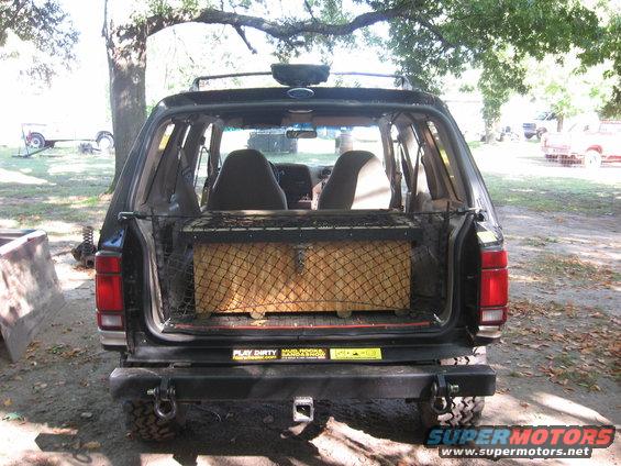 Black SUV rear view, open cargo area with net-covered box, aftermarket bumper, two stickers on tailgate