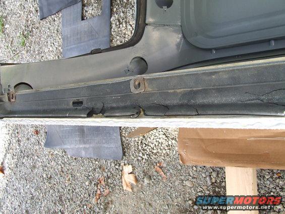 Close-up of a cracked and worn rubber door seal on a vehicle, resting on gravel