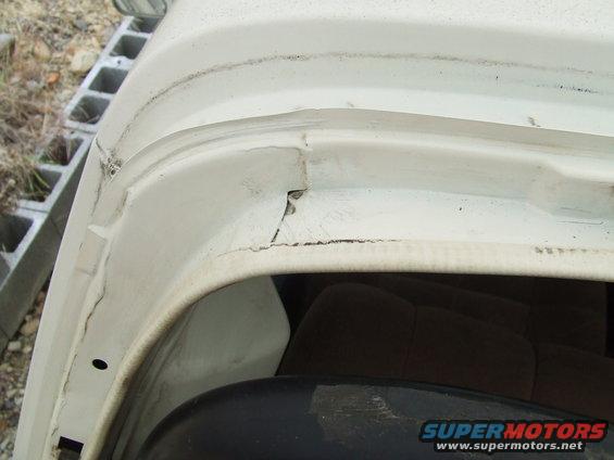 Close-up of white vehicle's upper door frame, showing some wear and tear. Interior seat visible