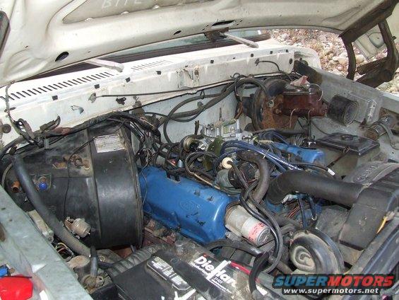 Engine bay with blue Ford valve covers, carburetor, and battery