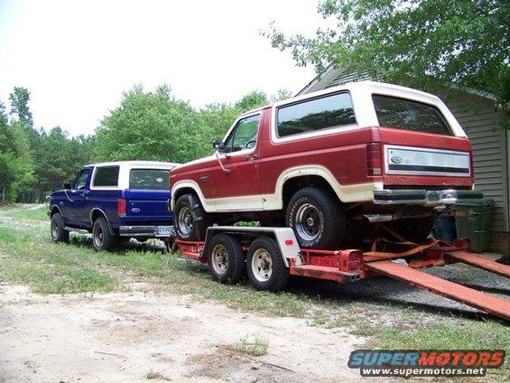 Red Ford Bronco on trailer, blue Bronco parked behind it