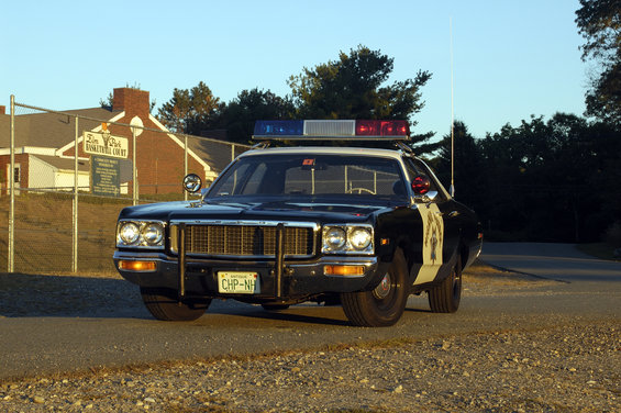 Black and white police car with light bar, front view. License plate reads CHP-NH