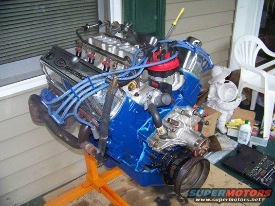 Blue V8 engine on an orange stand, with chrome valve covers reading "Ford Racing"