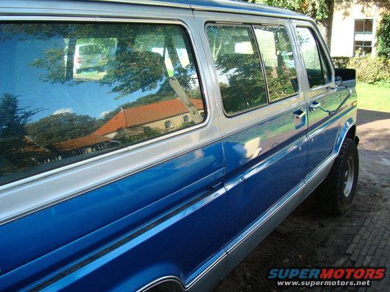 Blue and silver van, side view, with a reflection of another white van in the window