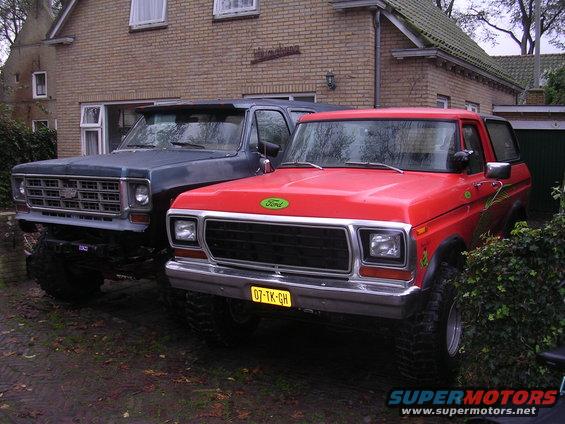 Red 1978 Ford Bronco with a yellow license plate parked next to a dark blue Chevrolet pickup truck