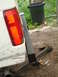 1989 Ford Bronco - The rear of a white vehicle is visible, a cracked taillight and a trailer hitch. A large trash can is in the background.